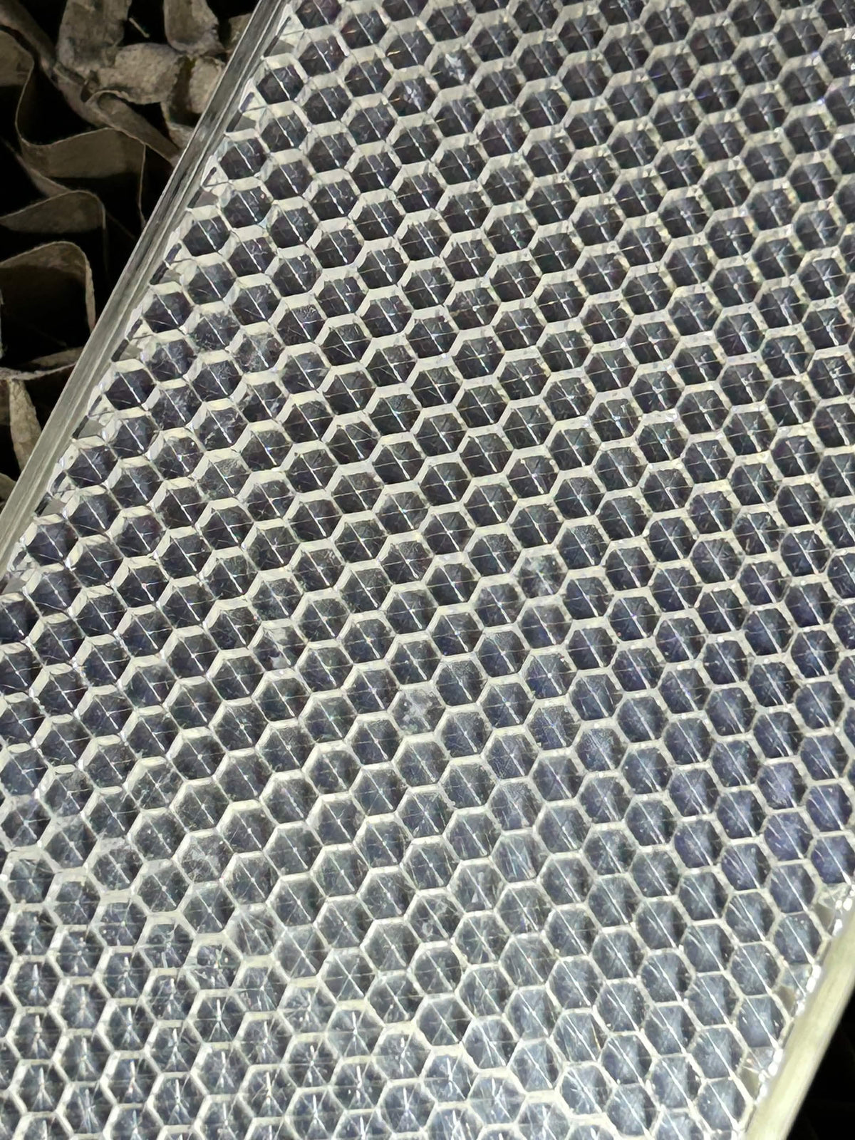 A close-up of a reflective silver honeycomb sheet with a metallic hexagonal pattern, showing some dust and scratches on its surface.